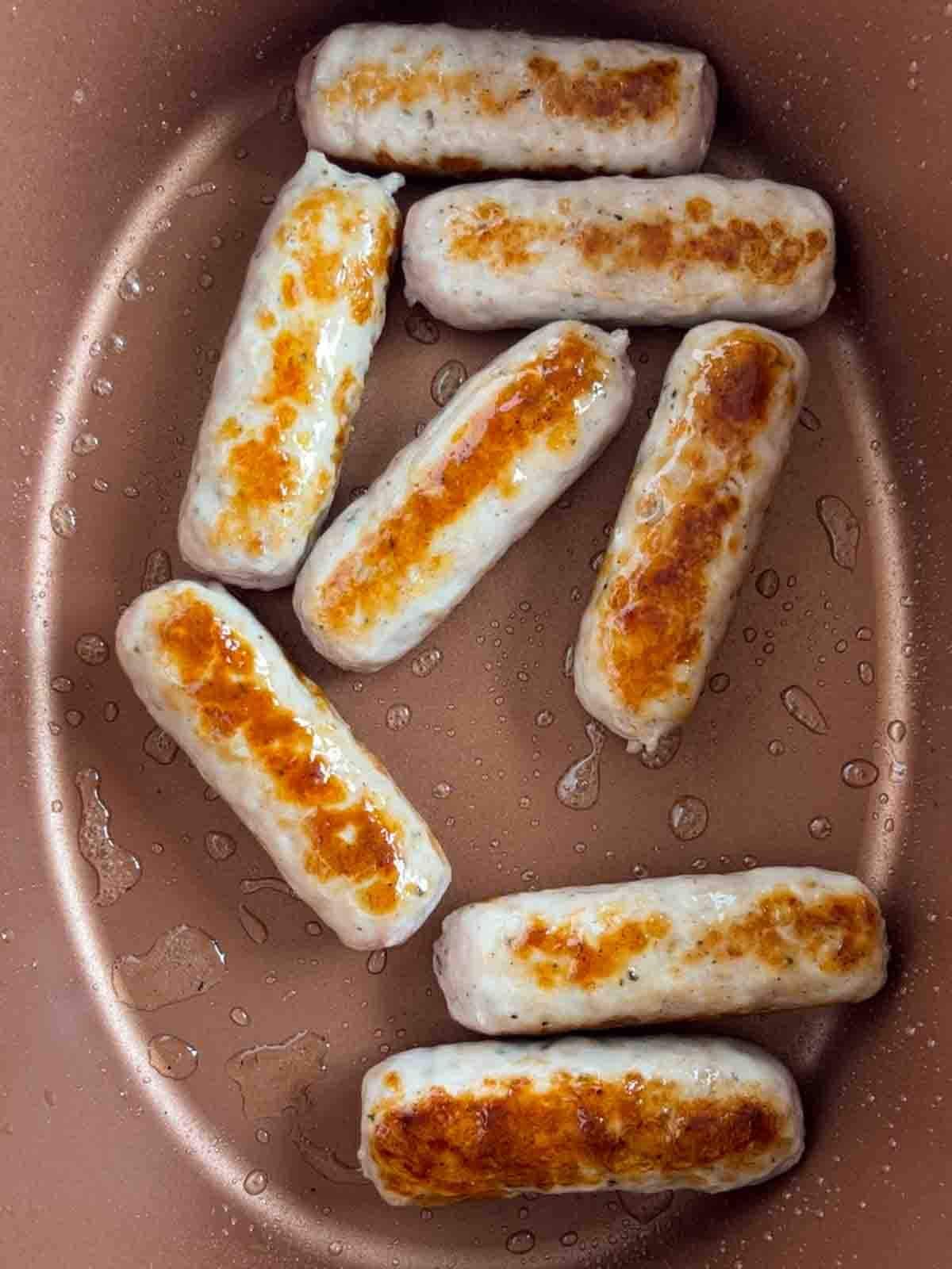 Sausages frying in a slow cooker for the recipe Sausage Casserole.