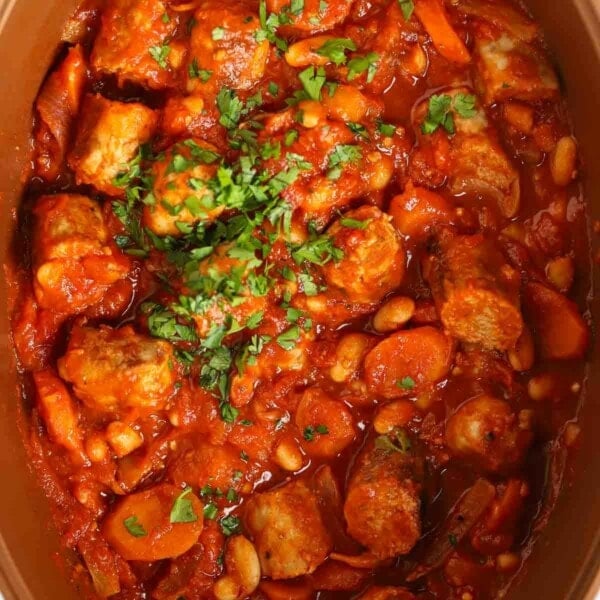 A close up image of a slow cooker sausage casserole, with chopped sausages, carrots and beans in a tomato sauce.