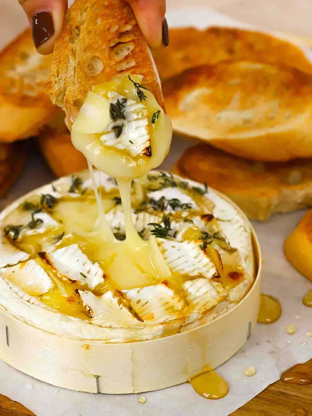 A baked camembert cheese with a hand dipping French crunchy bread into it as it oozes.