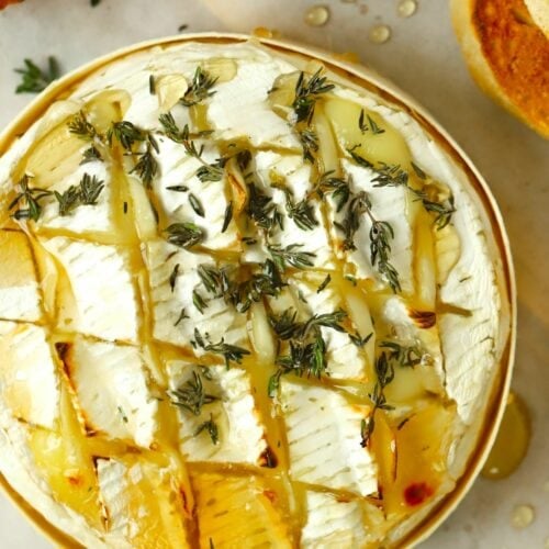 A baked camembert cheese in a wooden case, oozing with melted cheese and thyme on top. Lying next to toasted French bread.