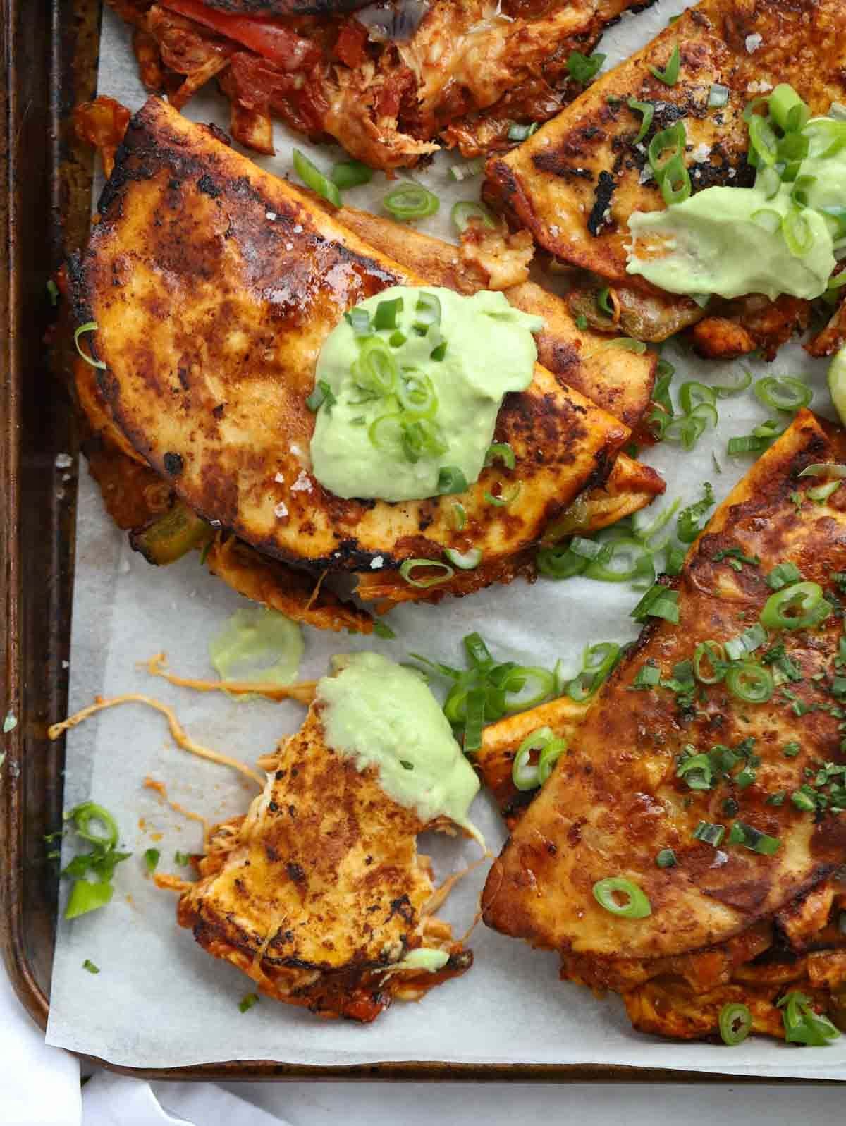 A tray with cooked chicken tacos, with a green dressing on the top and spring onions.