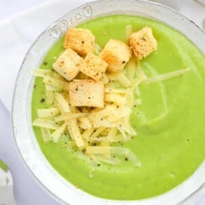 A bowl of green Broccoli and Cauliflower Soup with grated cheese and croutons on the top.