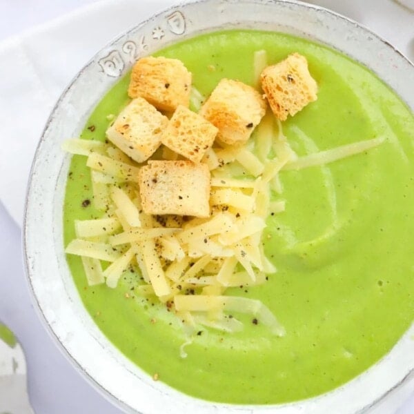 A bowl of green Broccoli and Cauliflower Soup with grated cheese and croutons on the top.