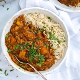 A bowl with butternut squash curry with rice and a fork ready to eat.