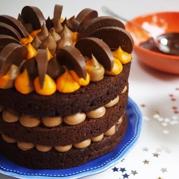 A layered chocolate orange cake on a plate with segments of Terry's Chocolate Orange on top.