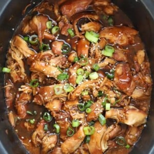 A slow cooker pan filled with a delicious Honey Garlic Chicken sauce, with spring onions sprinkled on top.