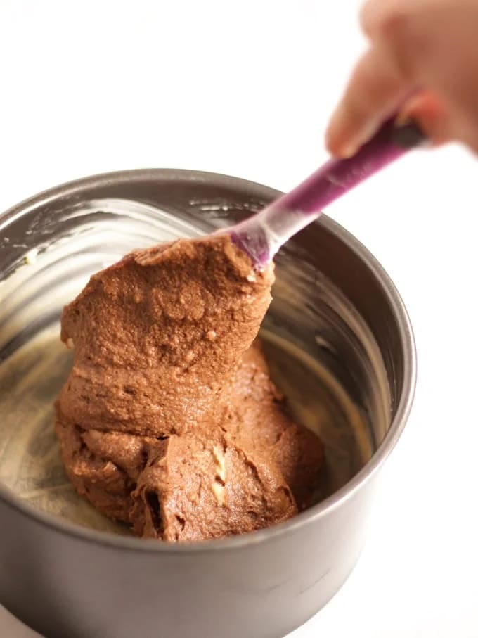 Raw chocolate cake mixture being spooned into a greased tin for step 2 in the recipe for Chocolate Orange Cake.