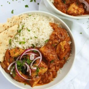 Two bowls of chicken curry and rice on a white tablecloth.