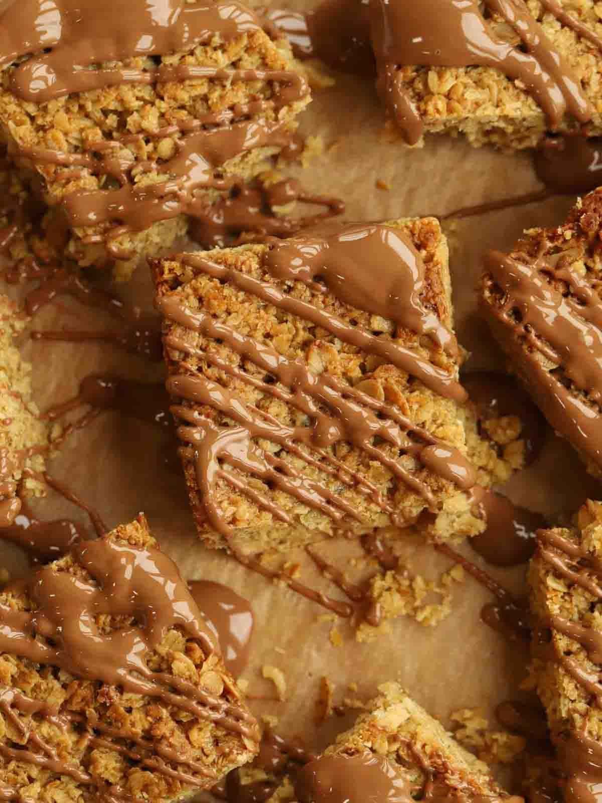 Squares of flapjack drizzled with melted chocolate on baking paper.