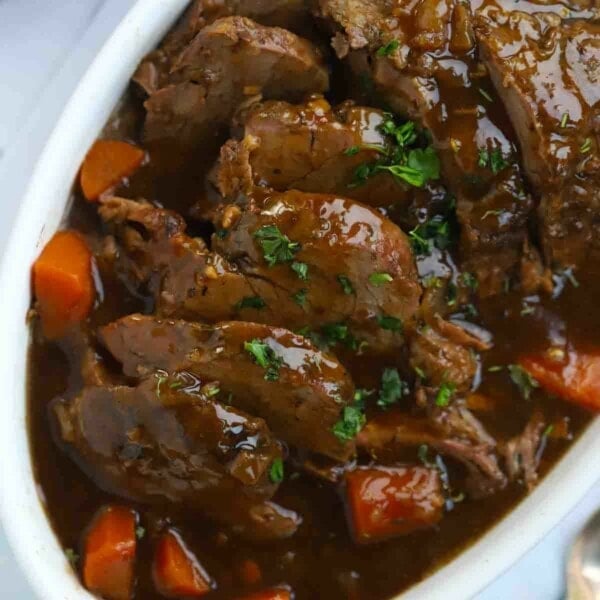 A cooked joint of beef in a serving dish, sliced and surrounding by carrots, in a rich dark gravy.