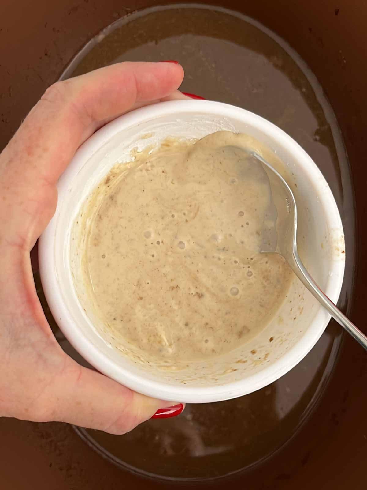 A little pot filled with a slurry and spoon stirring it, which is cornflour and gravy to make a thick paste to thicken the gravy.