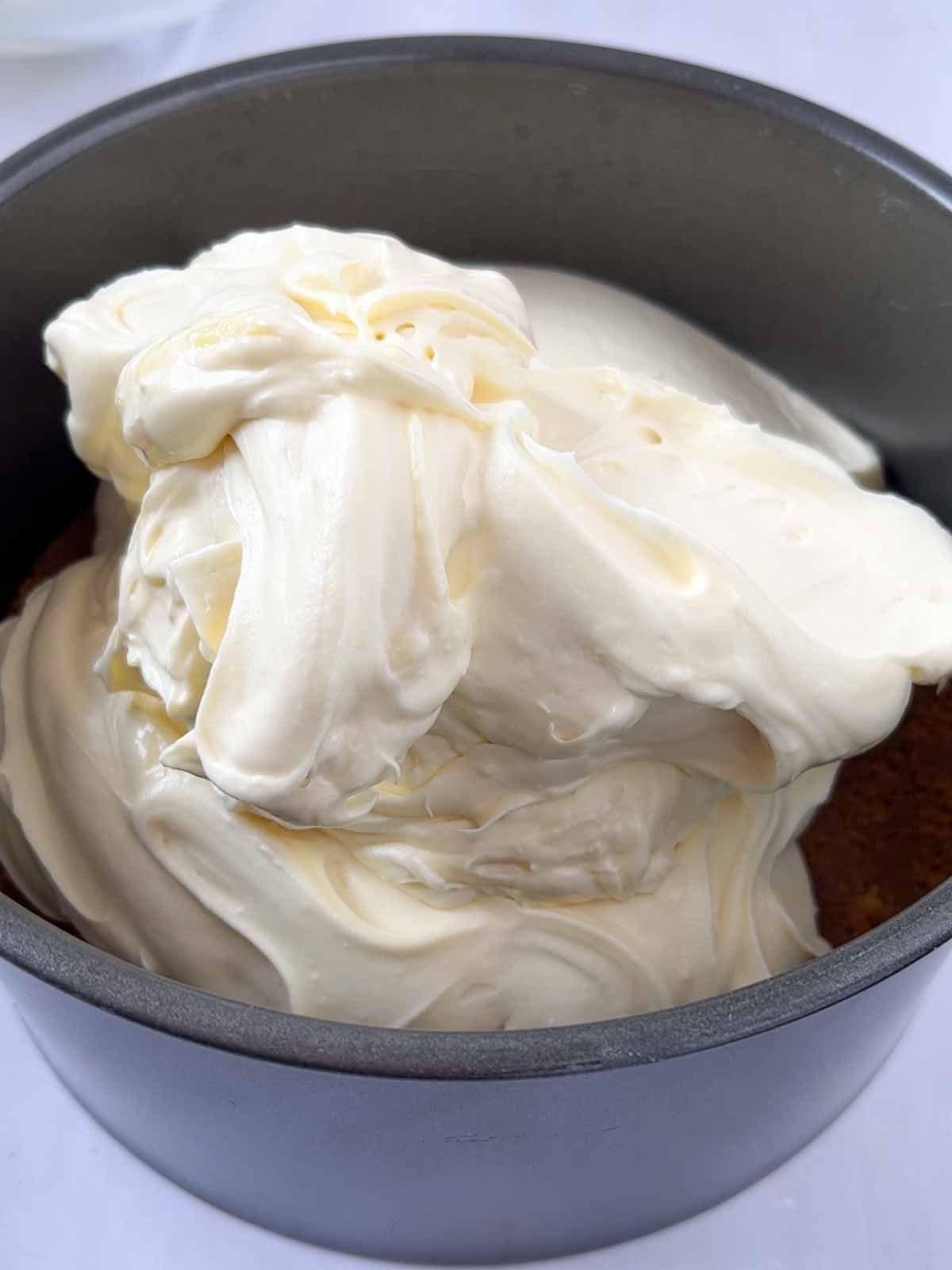 Whipped cream on top of a biscuit base for step 5 in the recipe for White Chocolate Cheesecake.