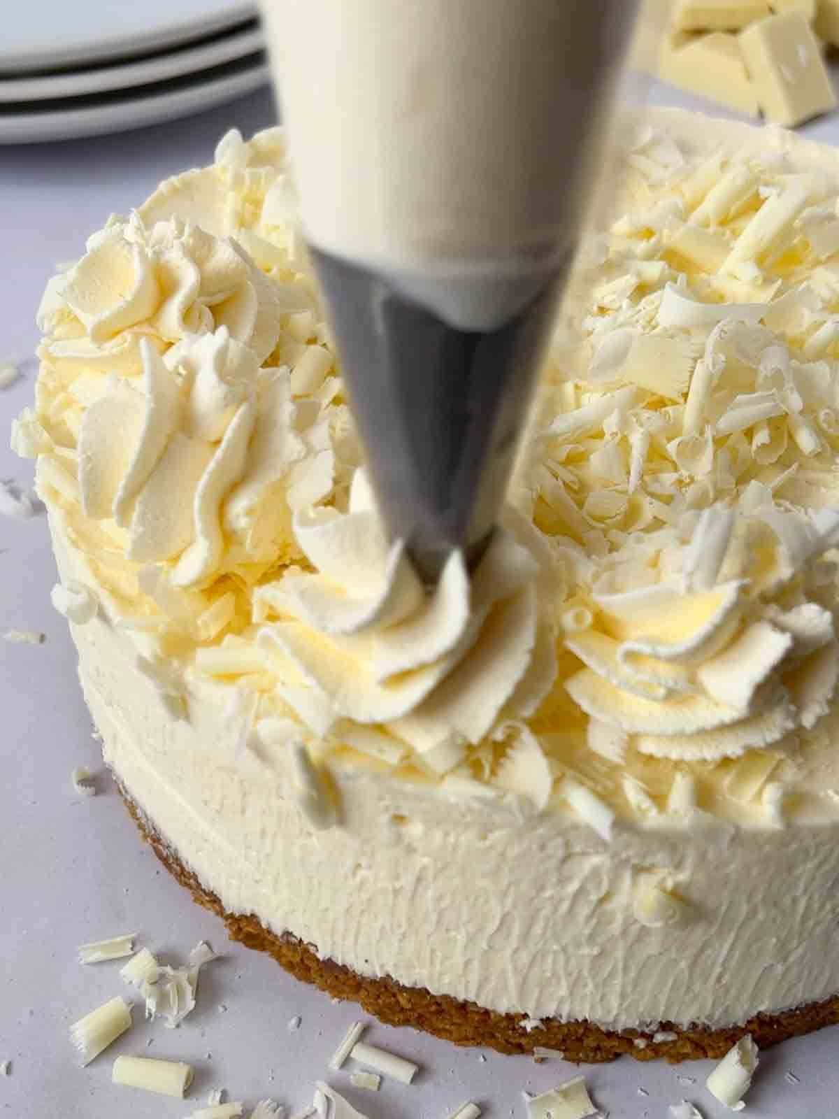 Creamy swirls being piped onto a white chocolate cheesecake.