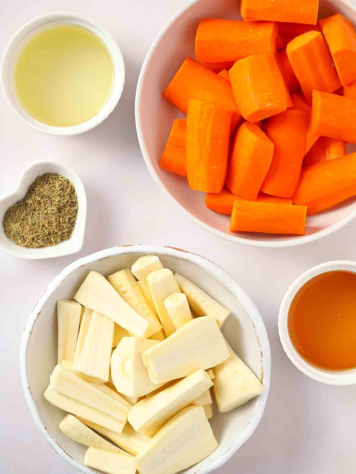 The raw ingredients for the side dish honey roasted carrots and parsnips laid out on a white counter.