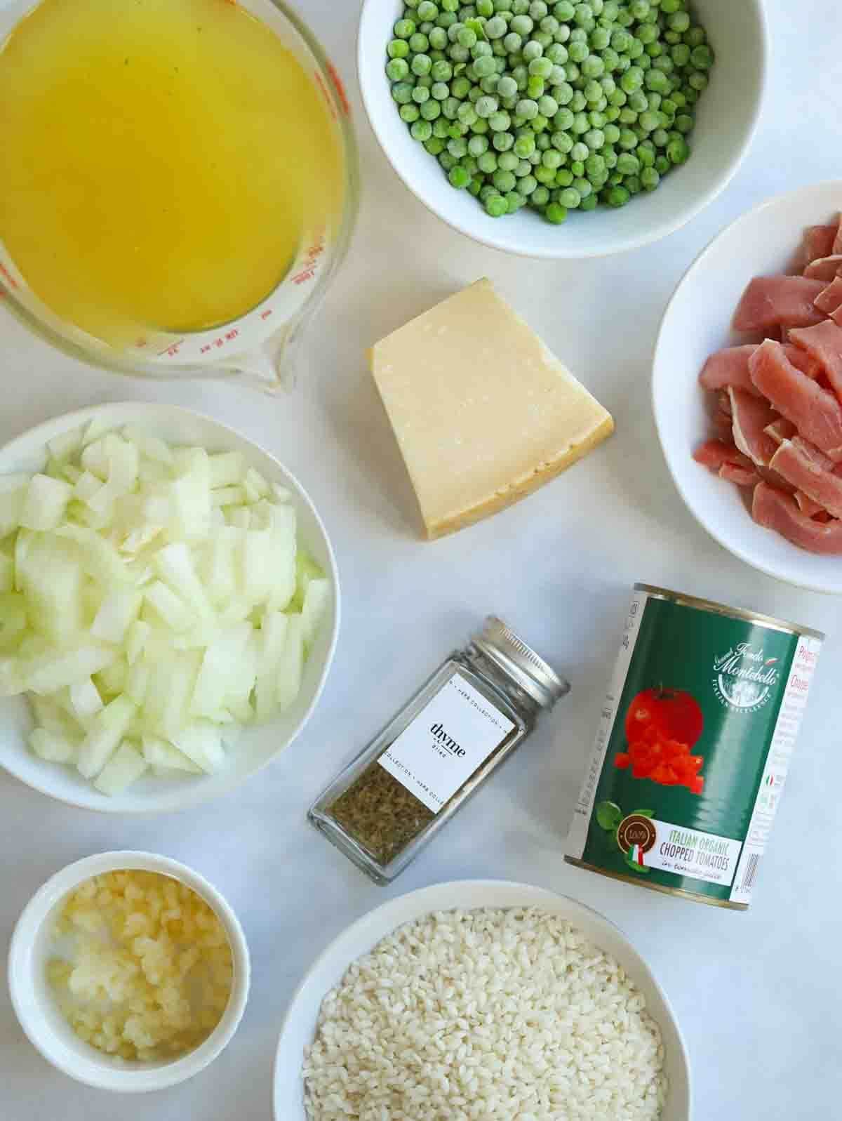The ingredients for oven baked risotto laid out on a counter top, including peas, bacon, rice stock, tomatoes, parmesan, onion, garlic and thyme.