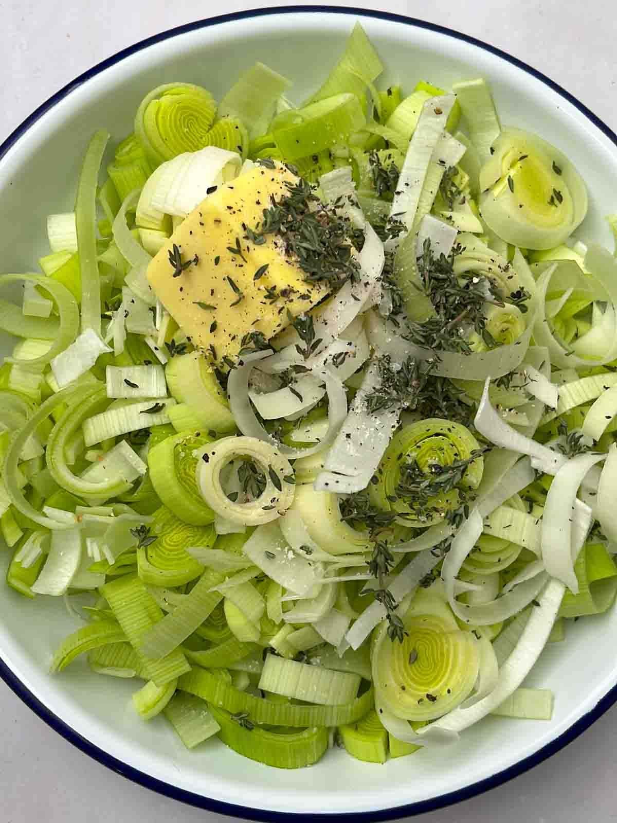 Leeks, butter and thyme in a dish, ready to go in the oven for the recipe for Mushroom Wellingtons.