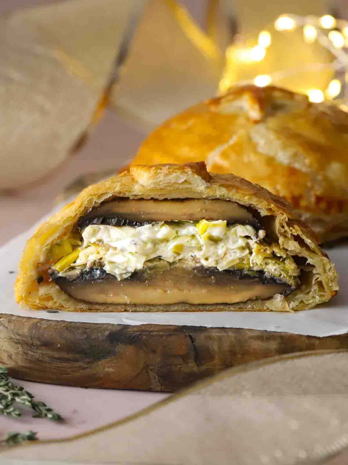 A mushroom wellington parcel on a board, sliced down the middle to show the filling.