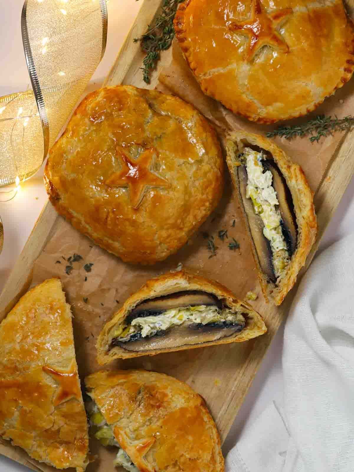 Mushroom wellingtons on a chopping board, one sliced down the middle to show the filling, with twinkly lights at the side and Christmas ribbon.