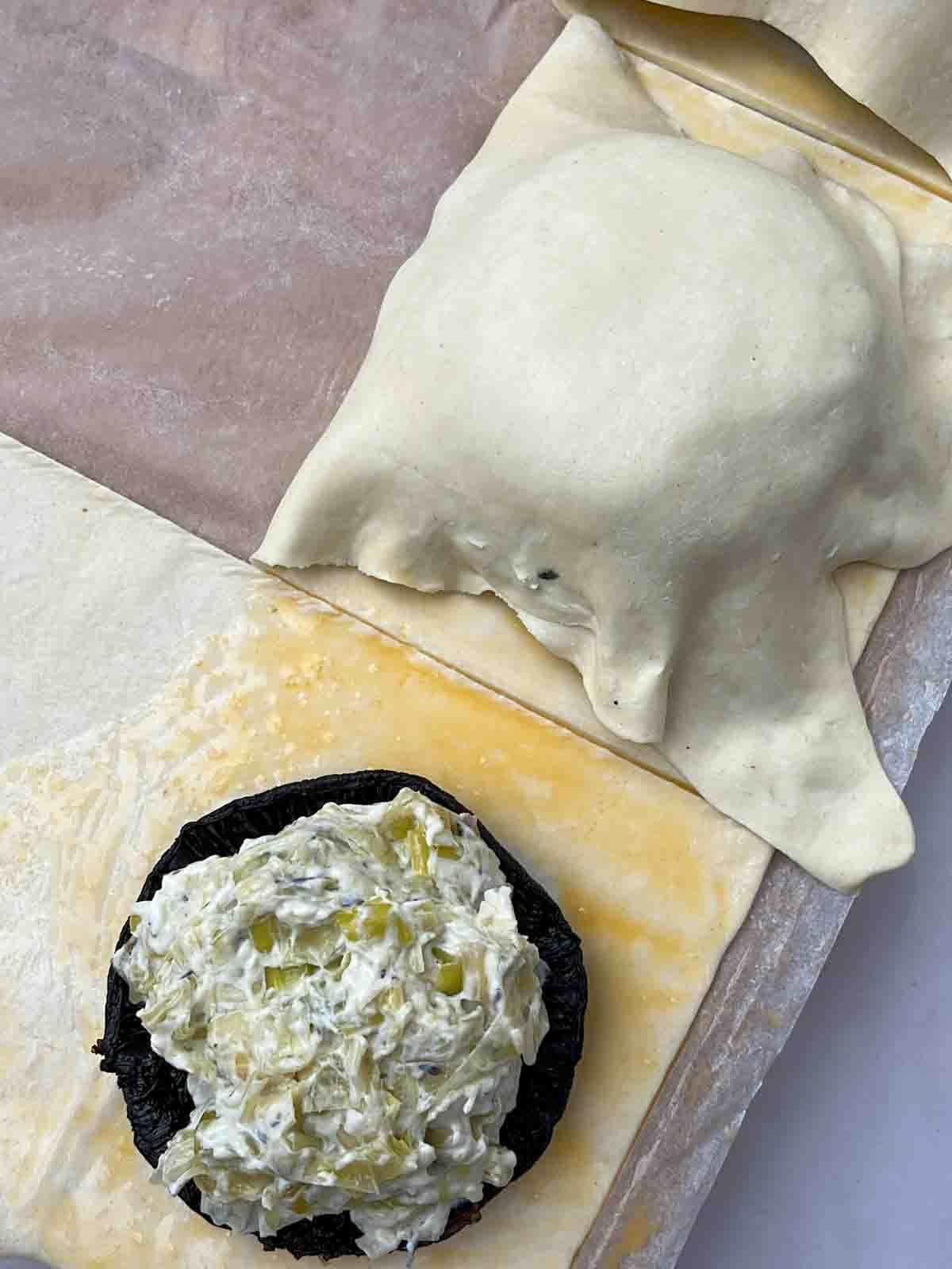 Step 5 in the process of mushroom wellingtons - one covered with pastry, the other with just the filling on top of the pastry strip.