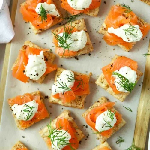 Smoked salmon square canapés on a serving plate with fill and creme fraiche on top.
