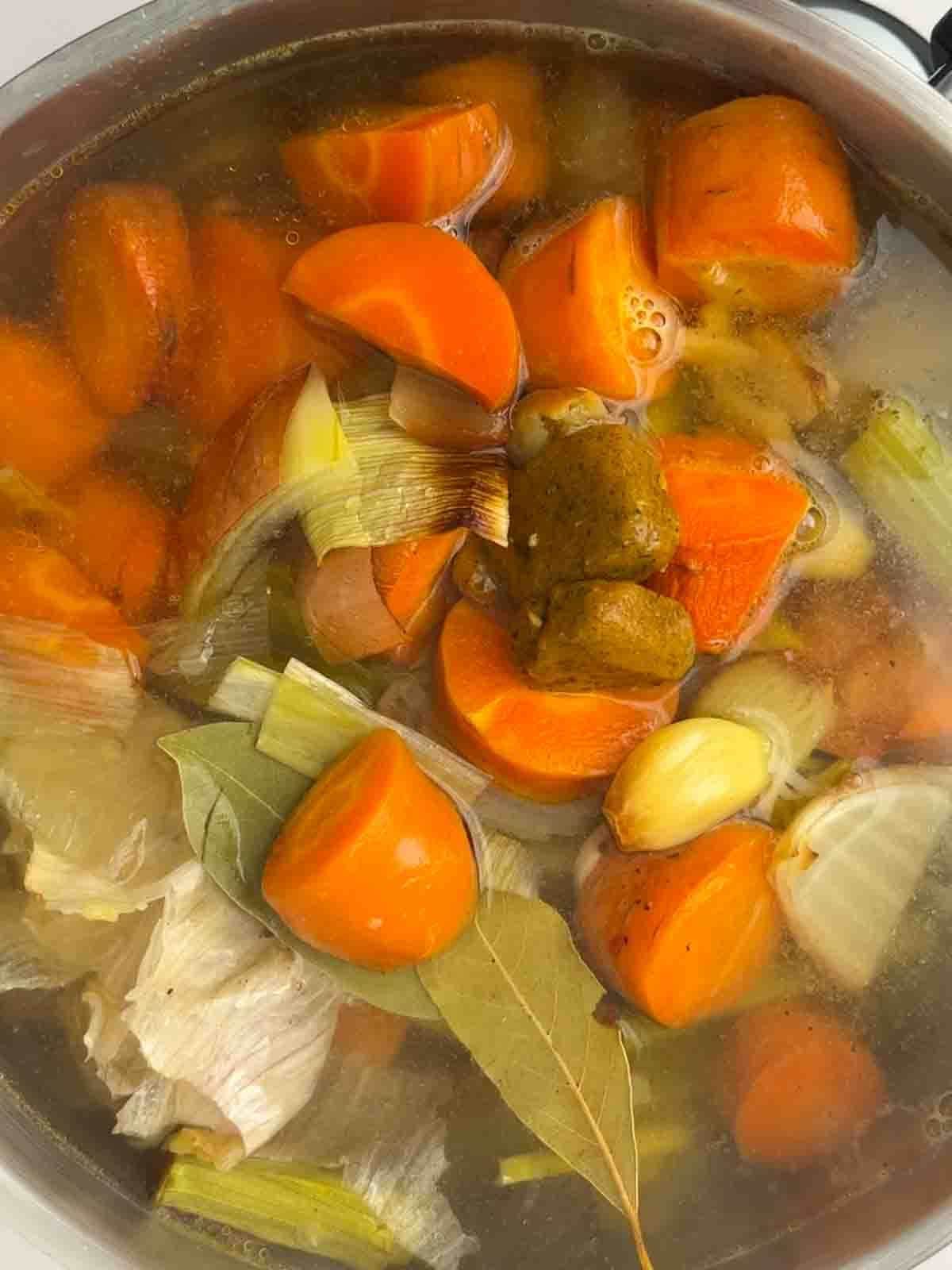 A mixture of vegetables and bay leaves in a pan of water with stock cubes for step 2 in the recipe for vegetarian gravy.