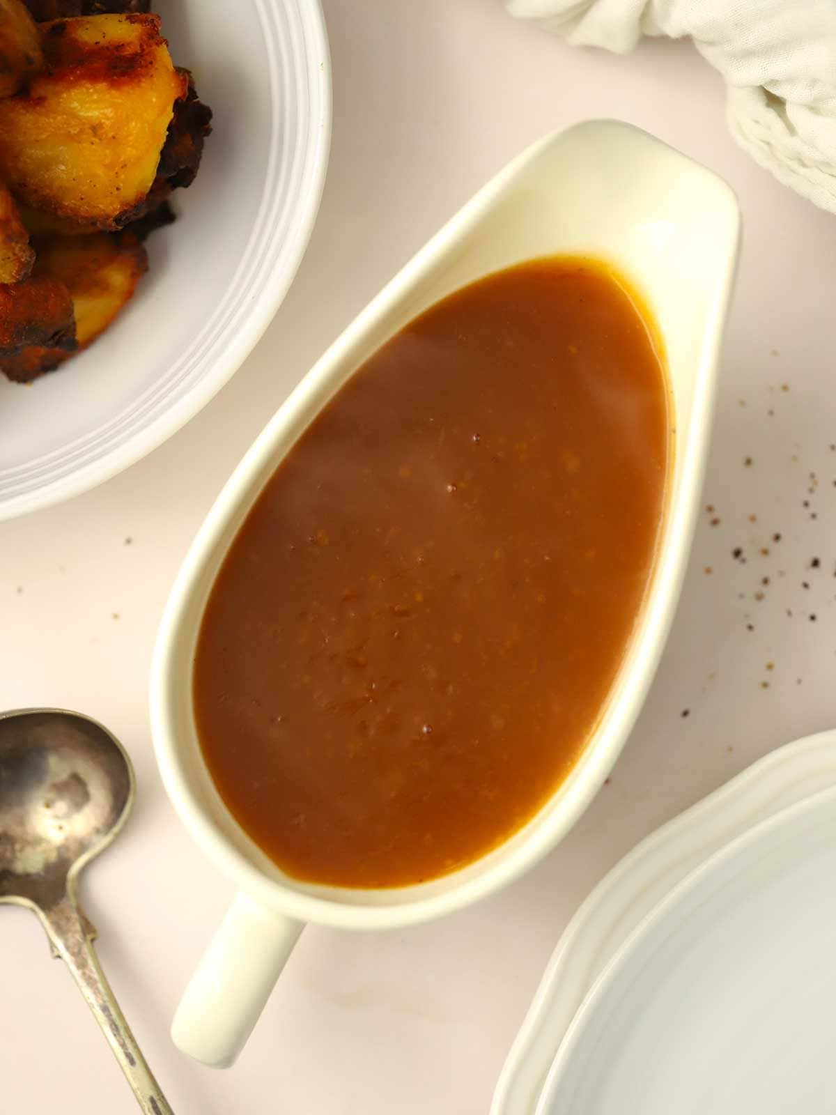 A bird's eye view of a gravy boat filled with thick vegetarian gravy, with roast potatoes just inside the image.