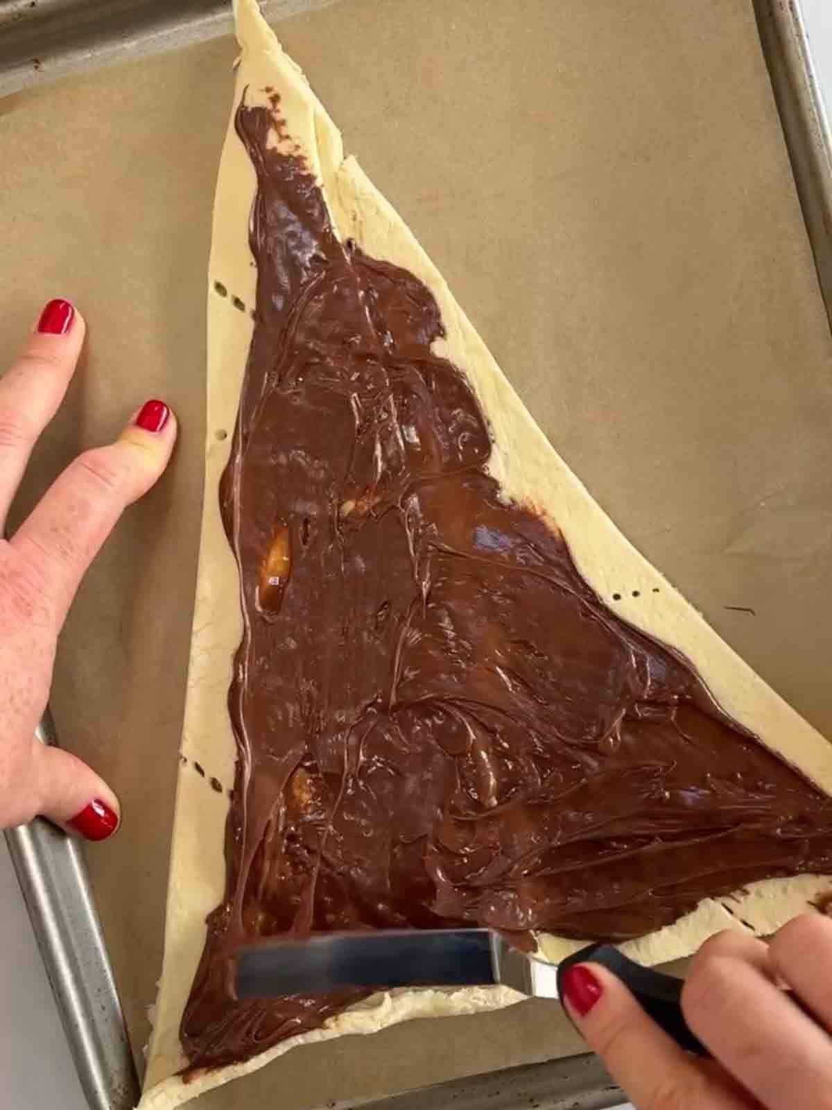 A triangle of croissant dough being smothered with nutella for the recipe Nutella Christmas Tree.
