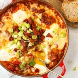 A big pan full of Shakshuka, ready to serve, with crusty bread on the side for dipping.