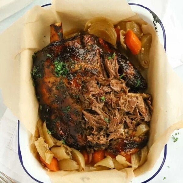 A roasted lamb shoulder cooked in the slow cooker, in a tin with baking paper, carrots and onion and a mint glaze on top.