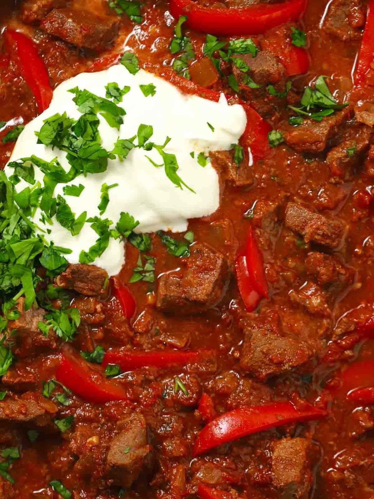 A close up of beef goulash with red pepper in a rich sauce.
