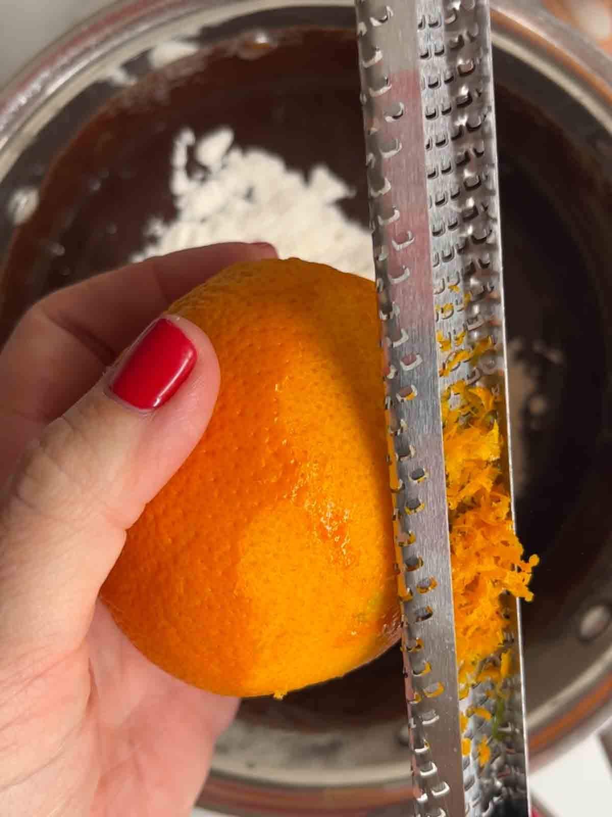 An orange being zested above a pan of melted chocolate for the recipe Terry's Chocolate Orange Brownies.