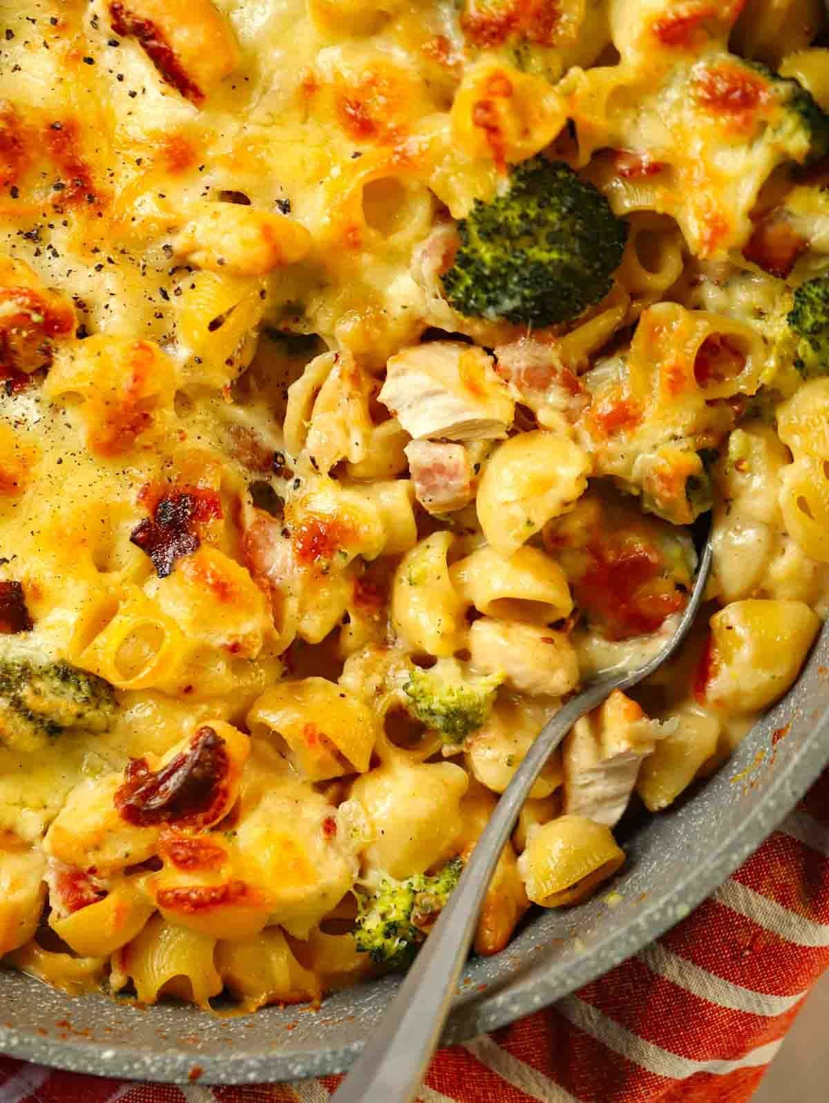 A bird's eye view of a corner of a pan filled with Chicken Pasta Bake, with a spoon stuck in, ready to serve.