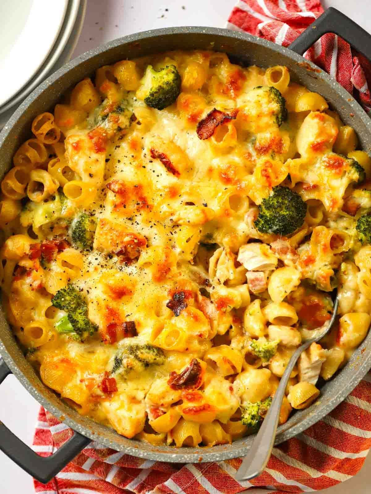 A big pan on a table filled with Chicken and Bacon Pasta Bake, with grilled cheese on top, ready to serve.