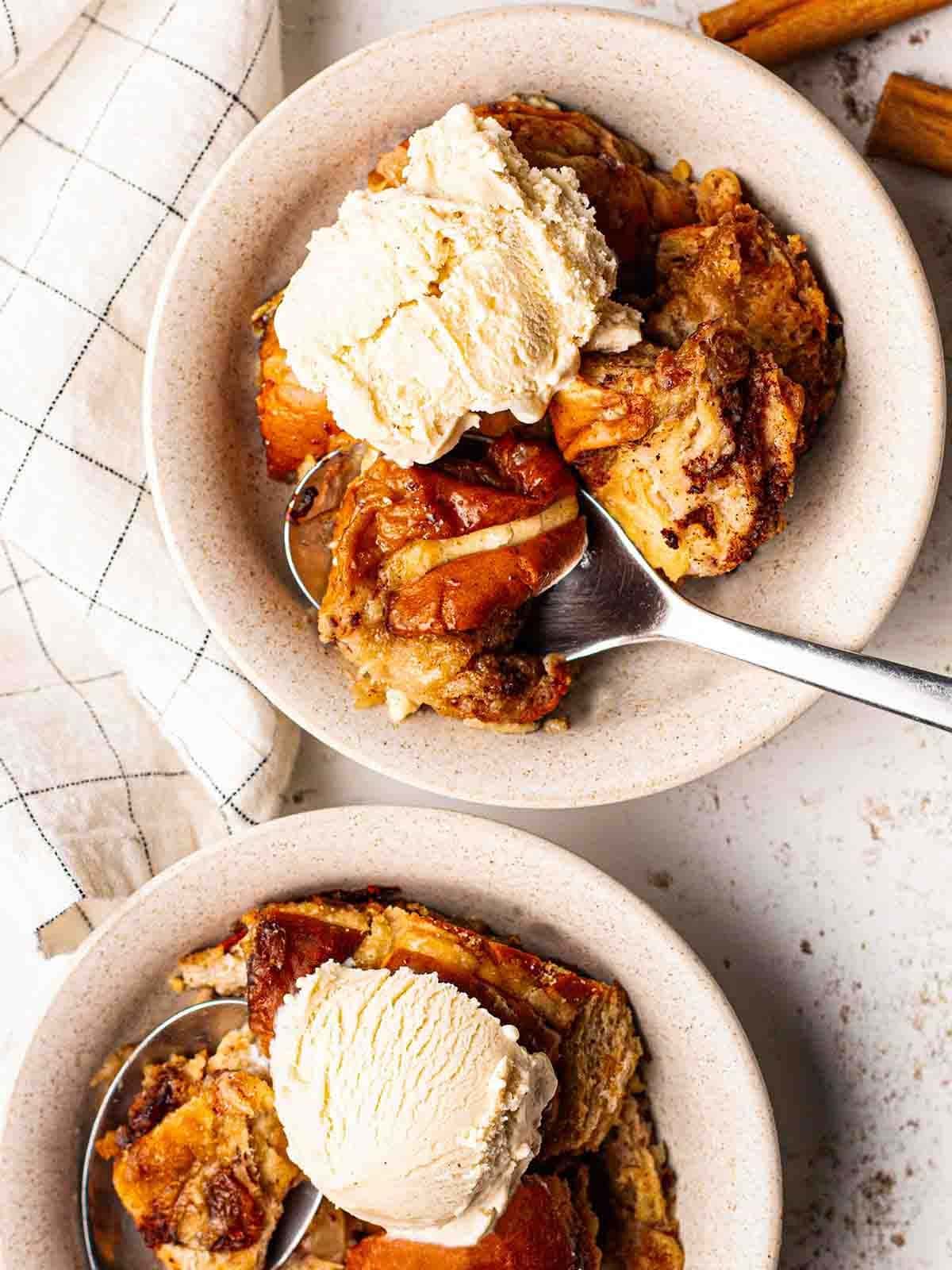 Two bowls with ice cream and cooked Hot Cross Bun Bread and Butter Pudding, with a spoon ready to eat.