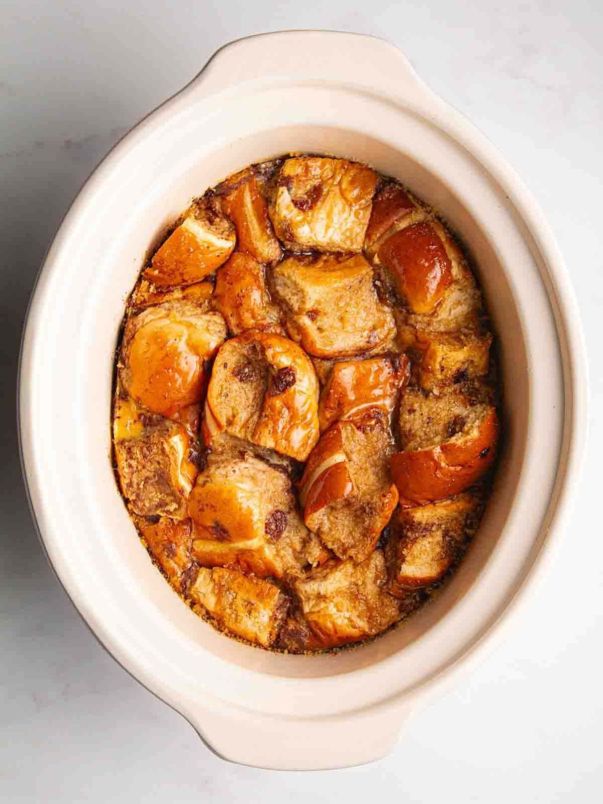 A slow cooker pan with cooked Hot Cross Bun Bread and Butter Pudding inside.