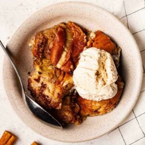 A bowl filled with hot cross bun bread and butter pudding and dollop of ice cream.