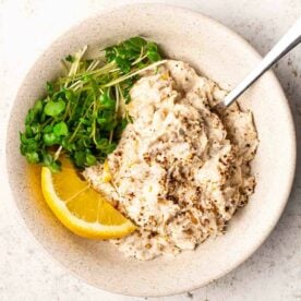 A plate filled with fresh mackerel pate, salad greens and a wedge of lemon, ready to be eaten with a fork in the pate.