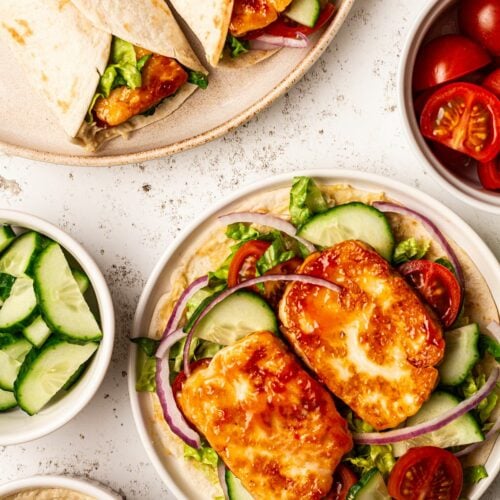 A table with plates of halloumi wraps and ingredients all around.