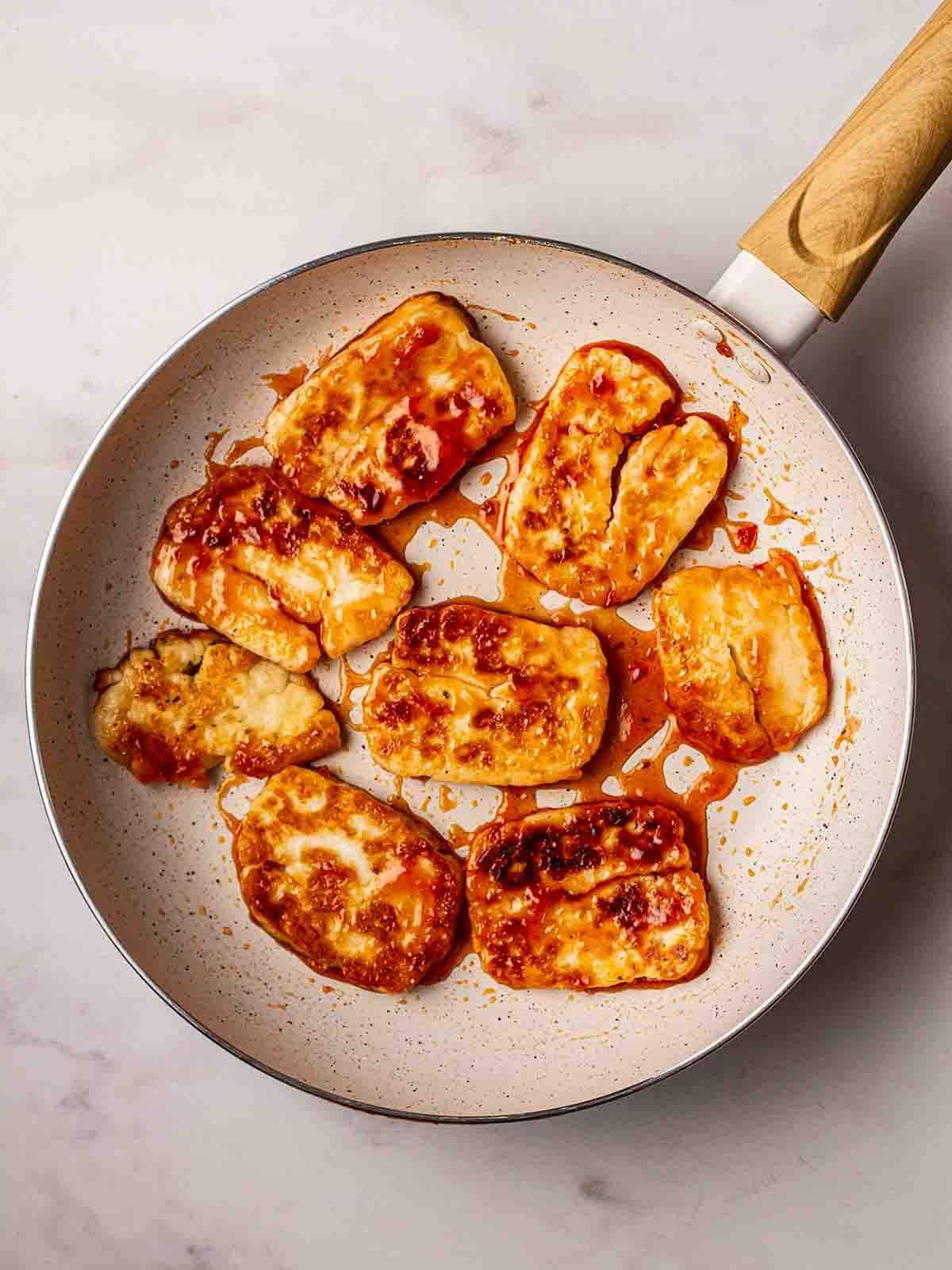 Slices of halloumi in a frying pan, being fried in red sweet chilli sticky sauce, for the recipe Halloumi Wraps.