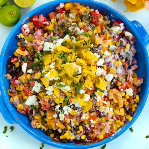 A big blue bowl filled with Mexican Salad, on a table surrounded with tortilla chips and limes.