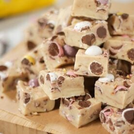 A pile of white chocolate mini egg fudge squares on a chopping board.