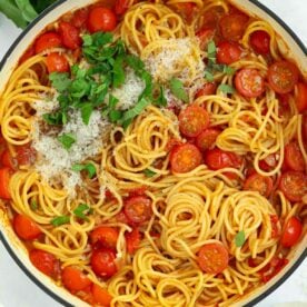 A big pan filled with cooked spaghetti and tomatoes, topped with parmesan and basil, for the recipe Tomato Pasta.