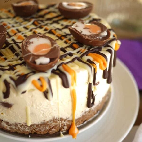 Cadbury's Creme Egg Cheesecake with dripping chocolate on a white plate with a purple background.