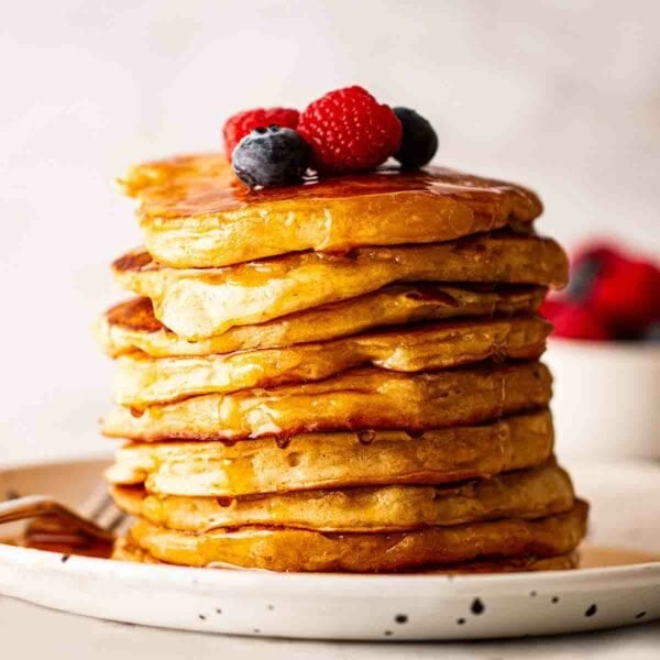 Golden, fluffy American Pancakes piled high on a plate with berries and syrup on top.