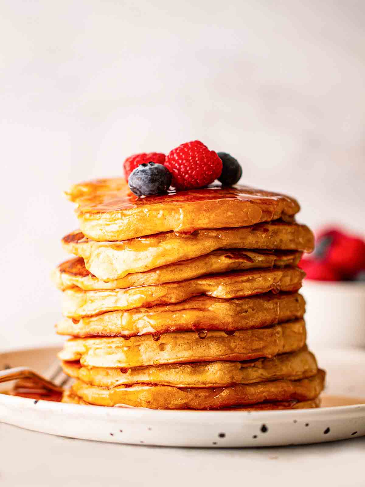 A pile of fluffy American Pancakes on a plate with blueberries and raspberries on top.