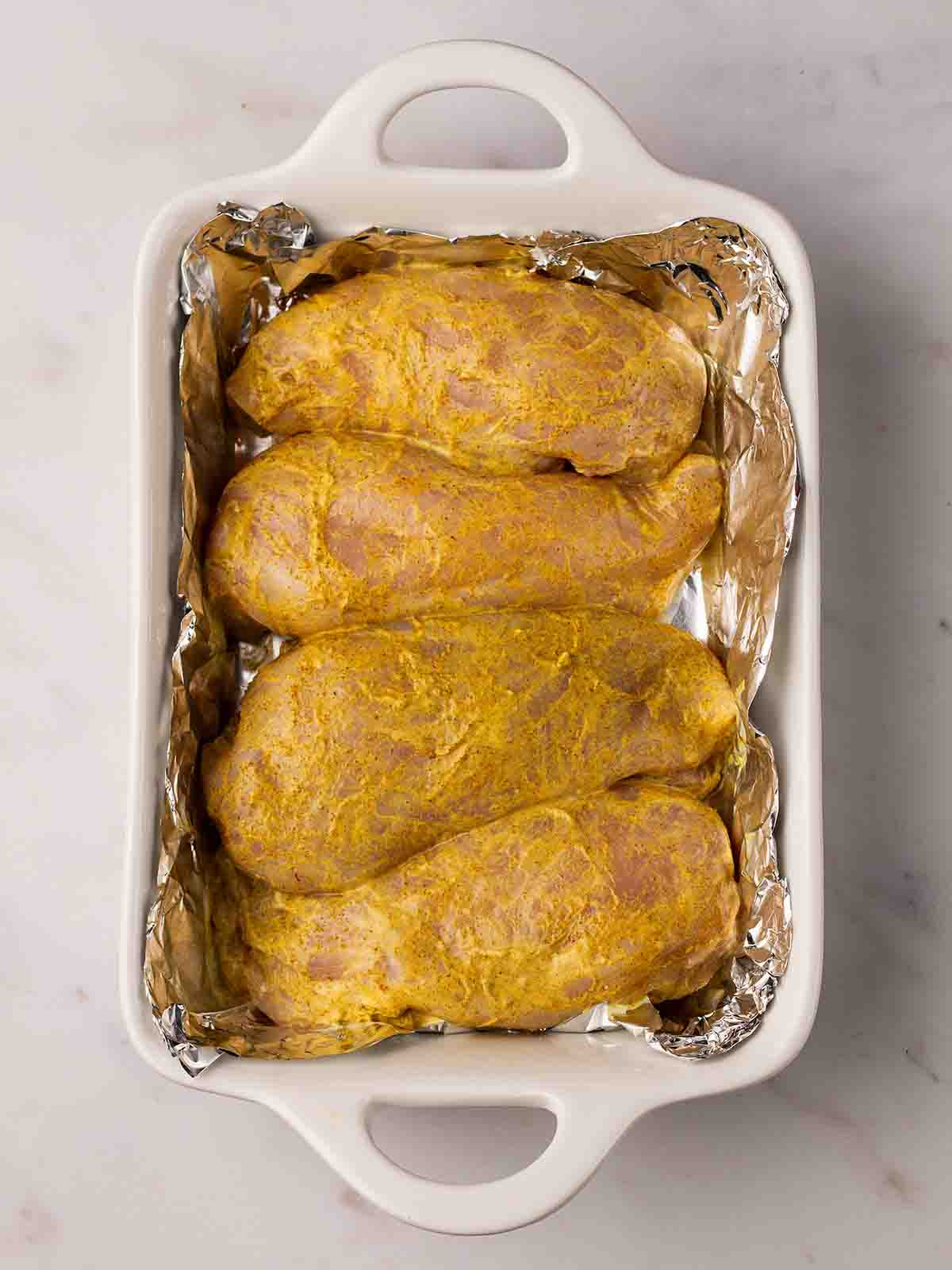 Four raw chicken breasts coated in Coronation Chicken marinade, ready to go in the oven.