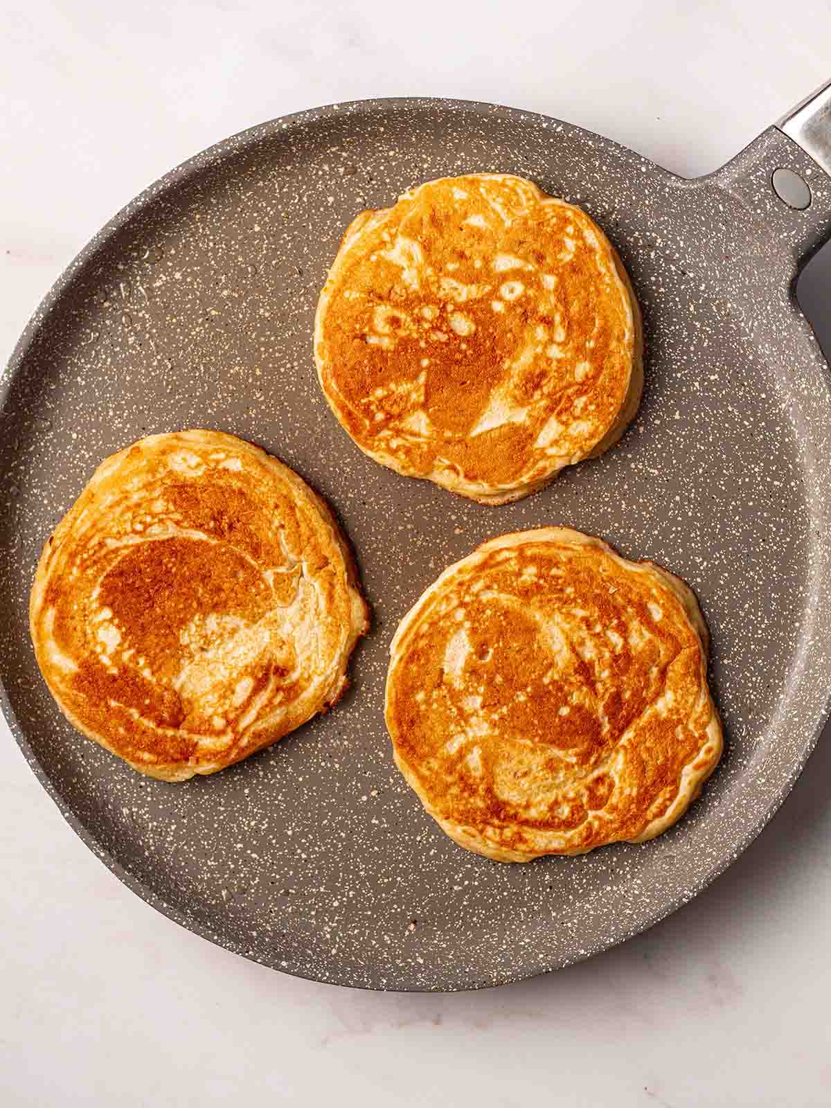 A frying pan with 3 round American Pancakes being cooked for step 4 in the recipe process.