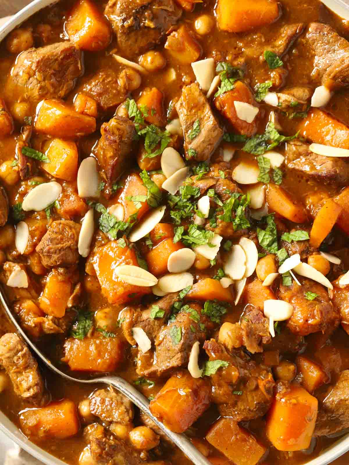 A big close up of a lamb tagine with almonds and mint on top.