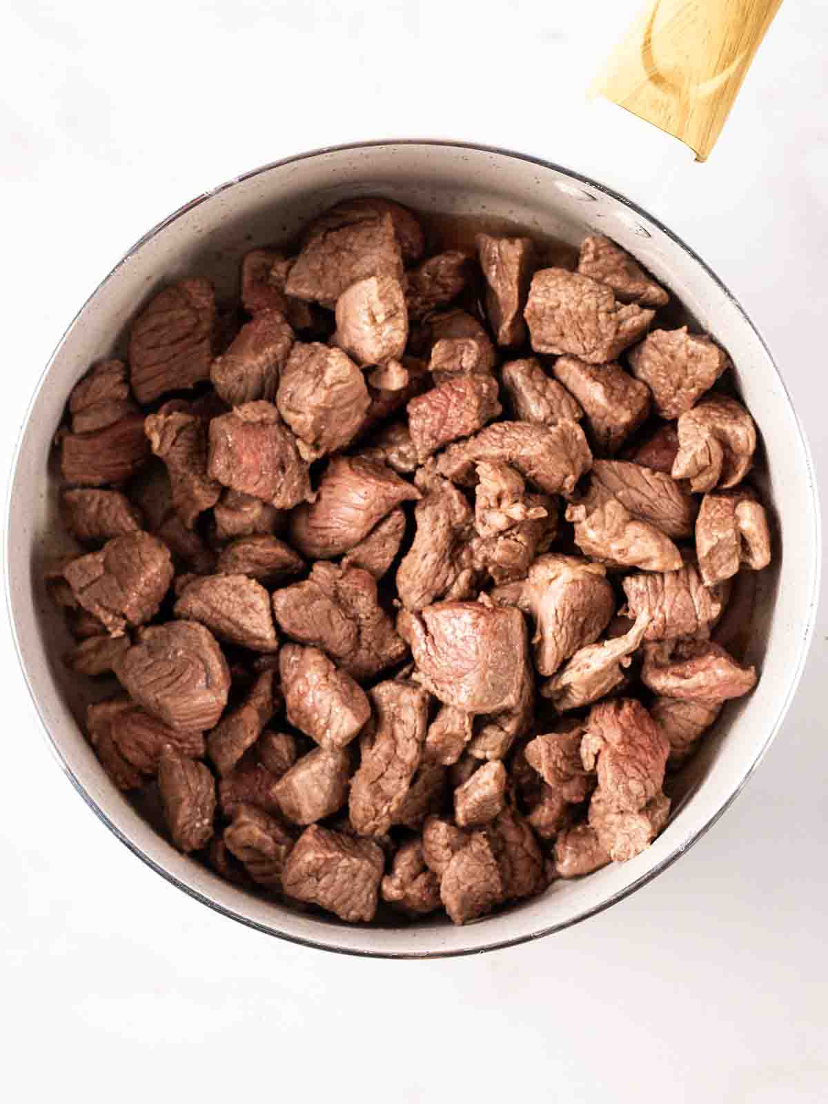 Browned lamb meat in chunks in a pan for step 1 in the recipe for Lamb Tagine.