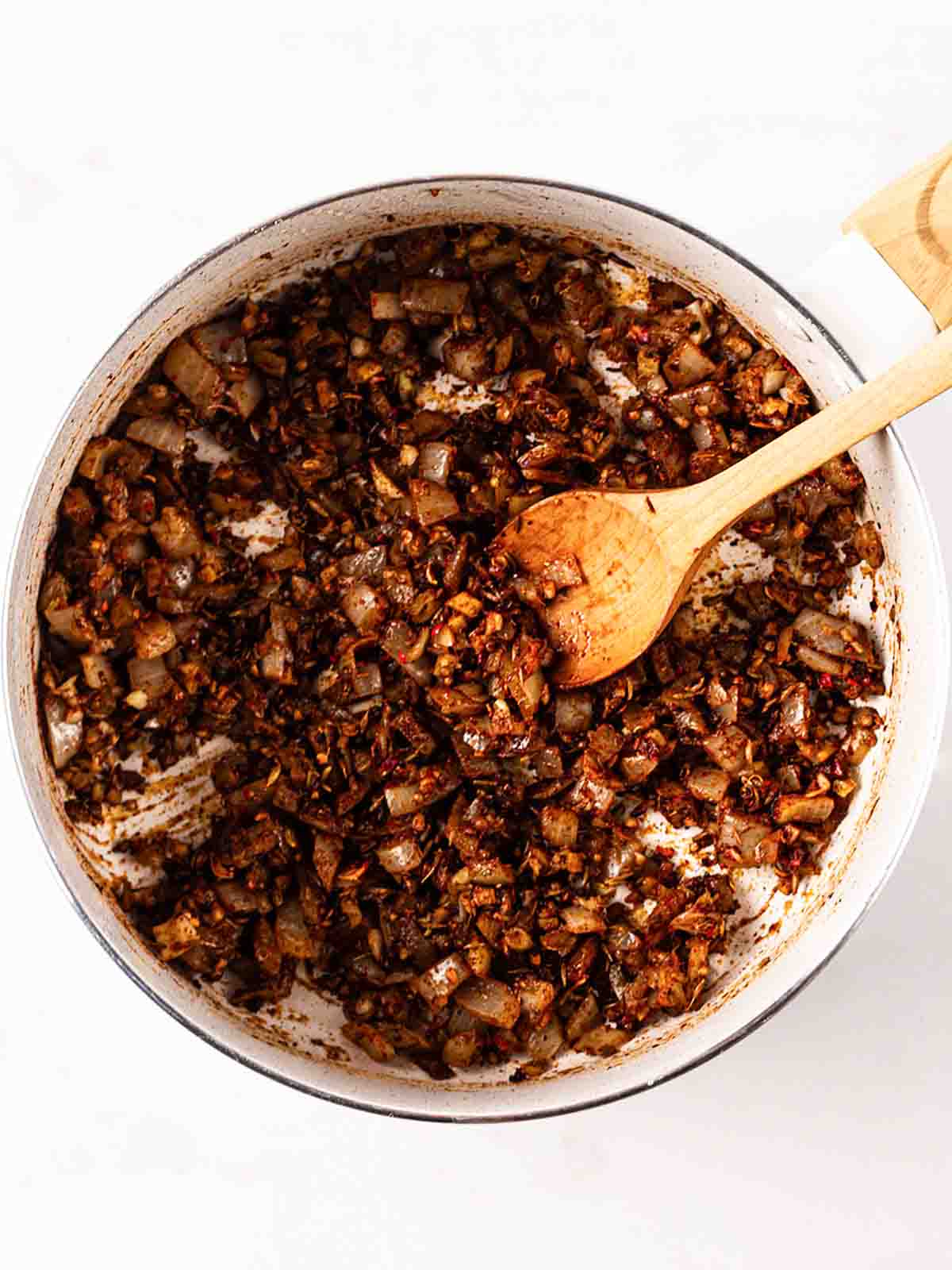 A large pan with onions and spices mixed together with a wooden spoon, for step 2 in the recipe for Lamb Tagine.